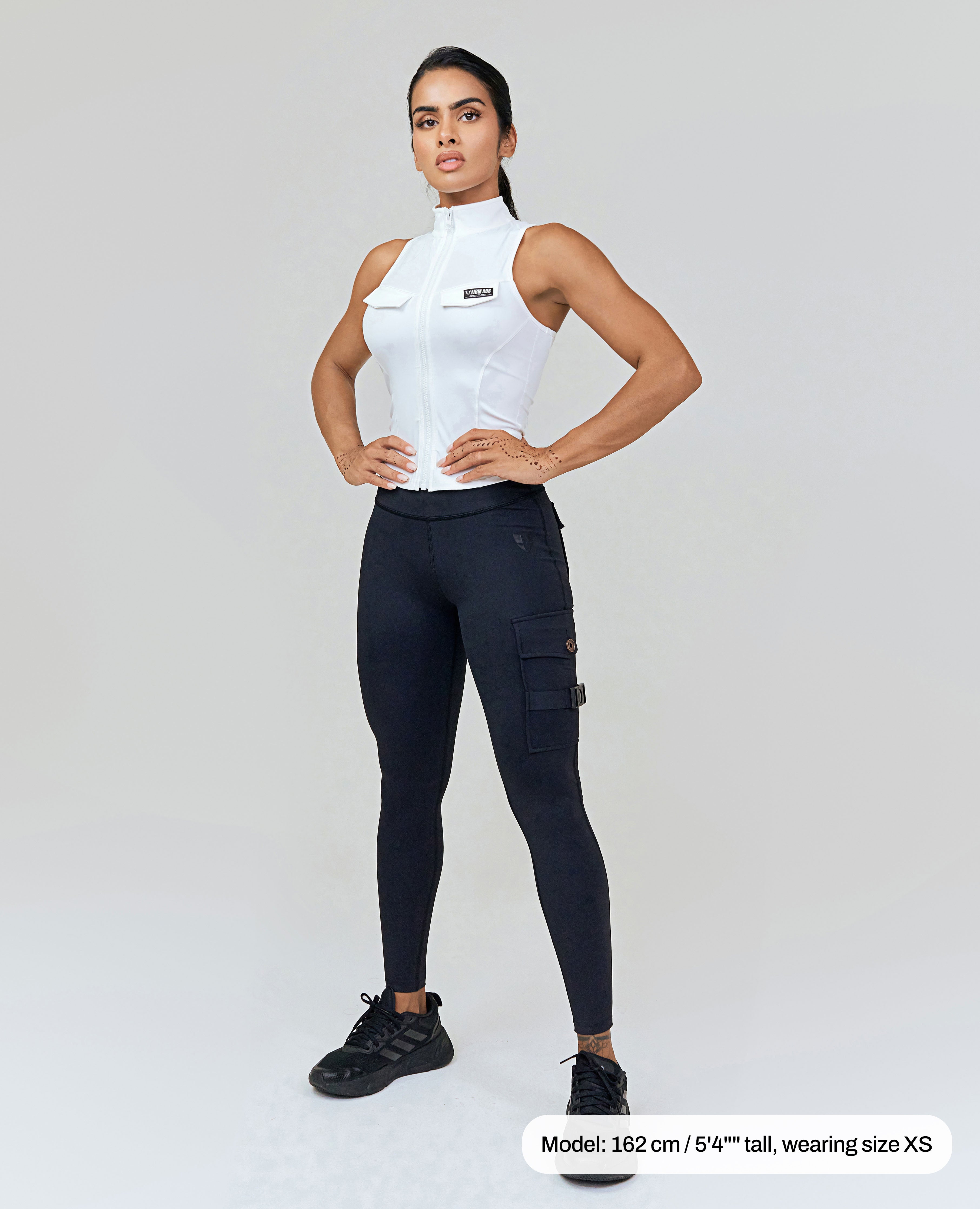 FIRM ABS white zip front sports tank worn by woman with black leggings and black sneakers