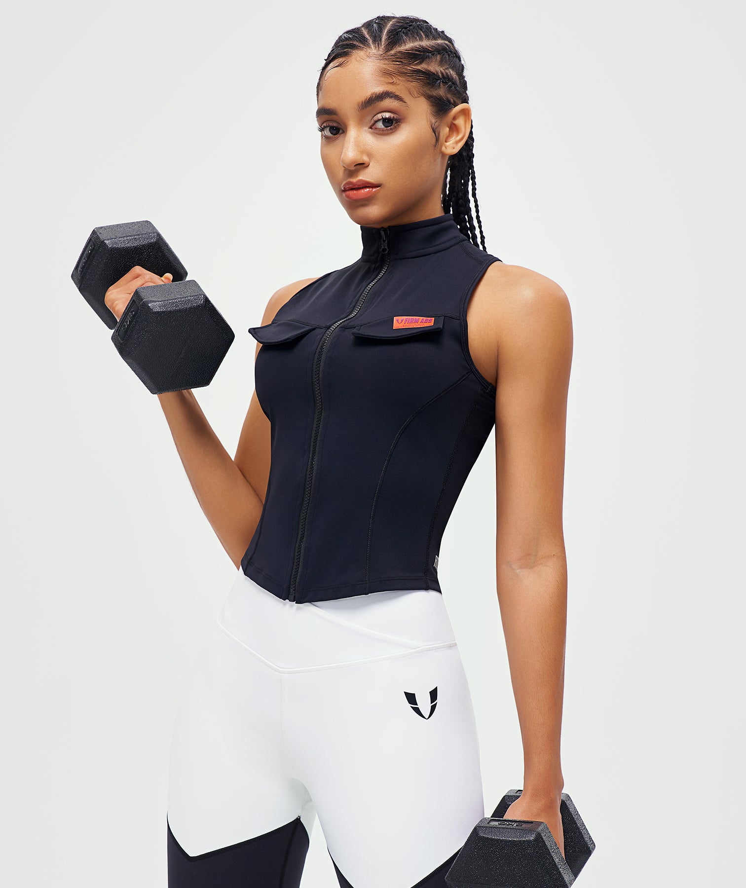 FIRM ABS black zip-up tank top as stylish workout top for women paired with white leggings lifting weights