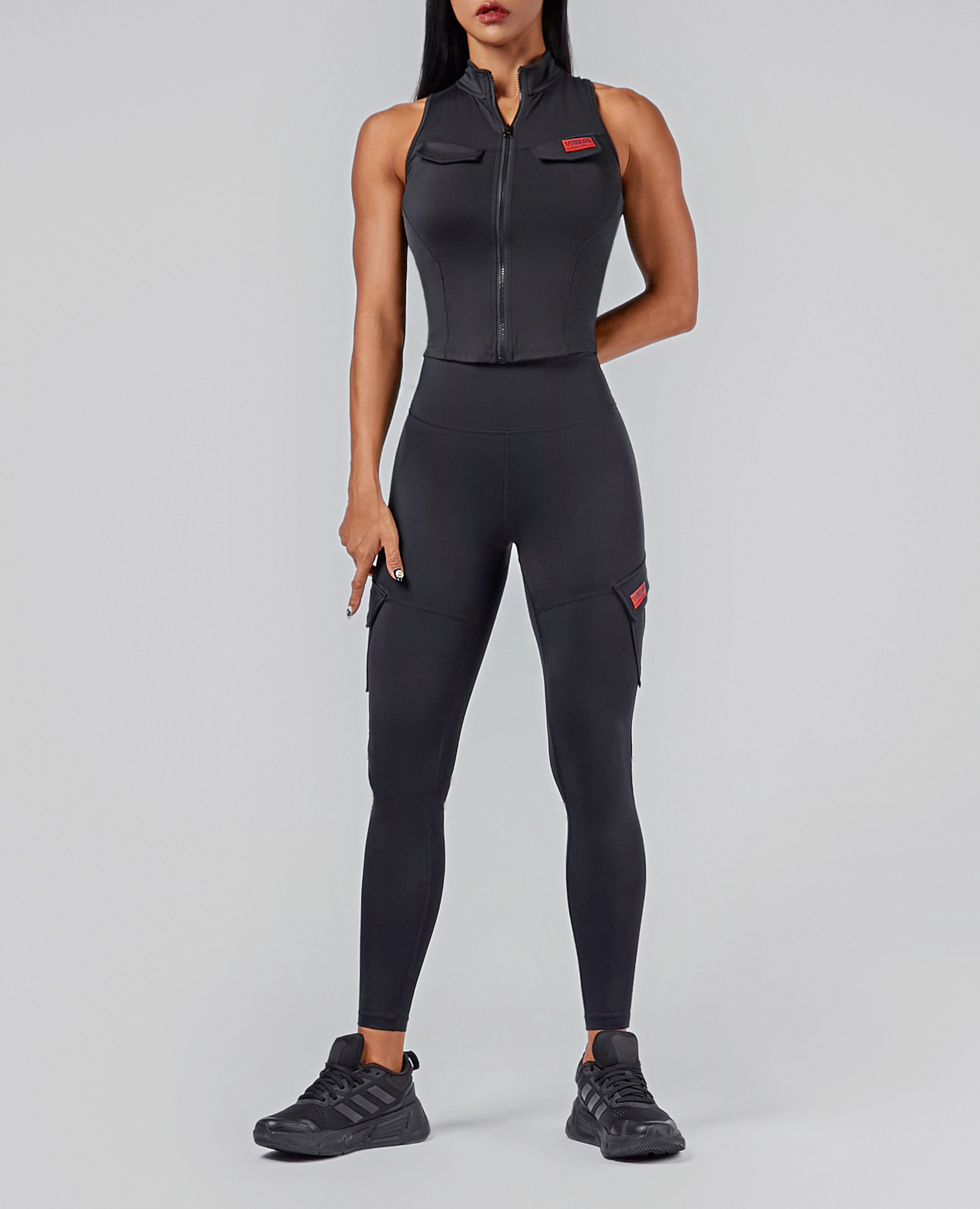 FIRM ABS high-waisted cargo leggings in black worn by model with zip-up sleeveless top and black sneakers